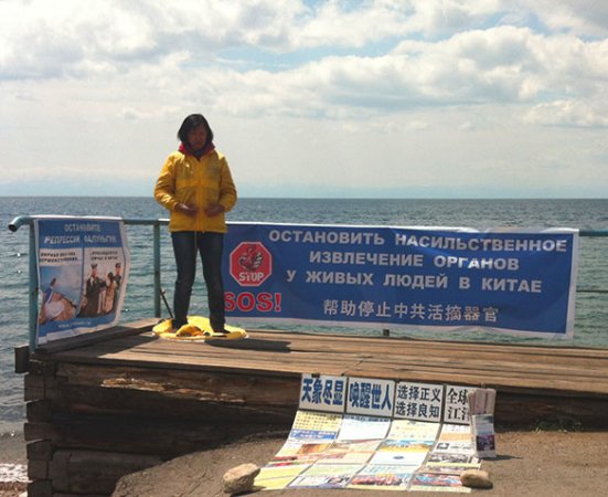 Надежда Лай на берегу Байкала выполняет упражнения Фалуньгун на фоне баннеров с информацией о преследовании практики в Китае