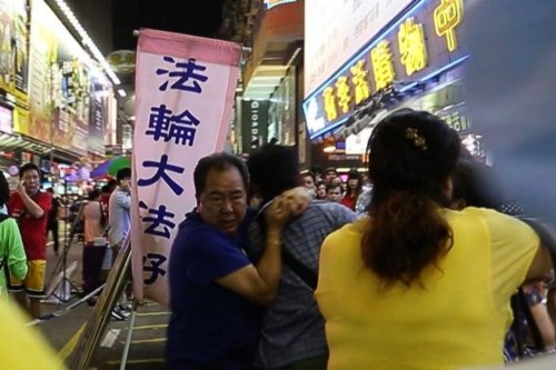 Линь Го-ань (в синей футболке слева), вице-президент Молодёжной ассоциации Гонконга, хватает прохожего за шею, а другой член HKYCA Сяо Сяожун пинает его