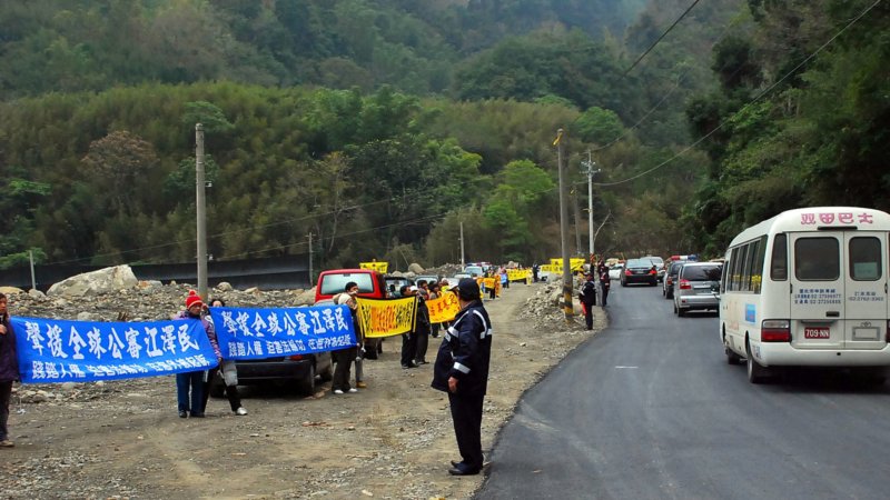 Последователи Фалуньгун стоят с плакатами вдоль дороги, по которой следует автоколонна Сюй Гуанчуня