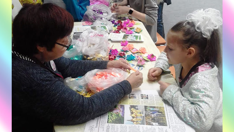 Девочка обучается изготовлению бумажного цветка лотоса, символа духовной чистоты