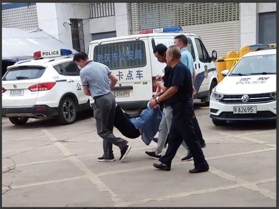 Полицейские несут Чжоу Айлинь к полицейской машине