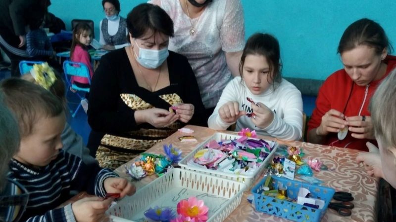 Дети и взрослые увлечённо складывают бумажные цветы лотоса