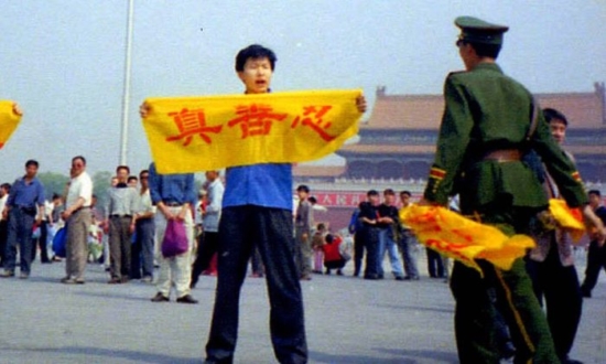 Практикующий Фалуньгун на площади Тяньаньмэнь с транспарантом, на котором написаны иероглифы Истина, Доброта, Терпение